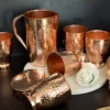 A handcrafted hammered copper jug and tumbler set with a polished, artisanal metal finish.