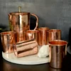 A handcrafted copper jug and tumbler set, featuring intricate engraving and a high-shine finish.