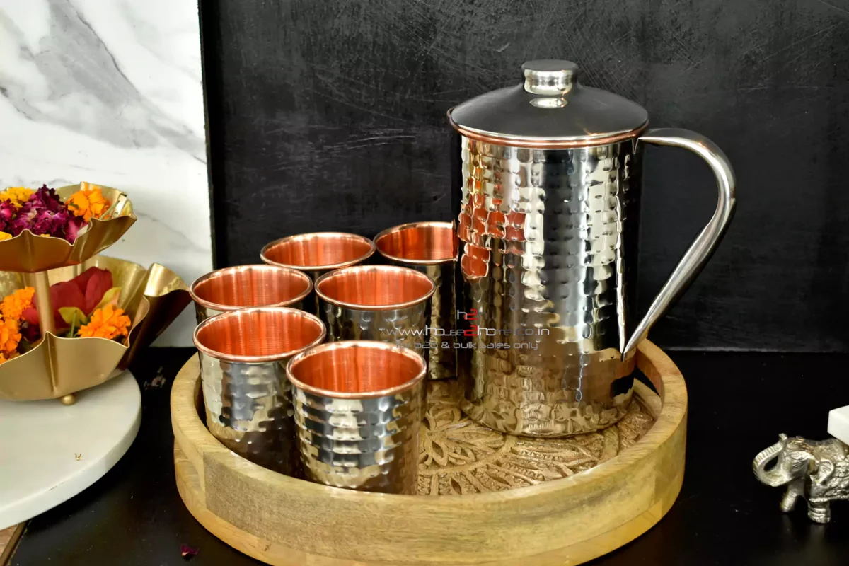 Hammered stainless steel and copper pitcher and tumbler set on a carved wooden tray for a premium kitchenware look.