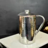 A gleaming, hammered stainless steel pitcher with a lid, offering a refined and durable metallic aesthetic.