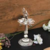 Ornate German silver peacock diya stand with hanging metal bells placed against a wooden backdrop.