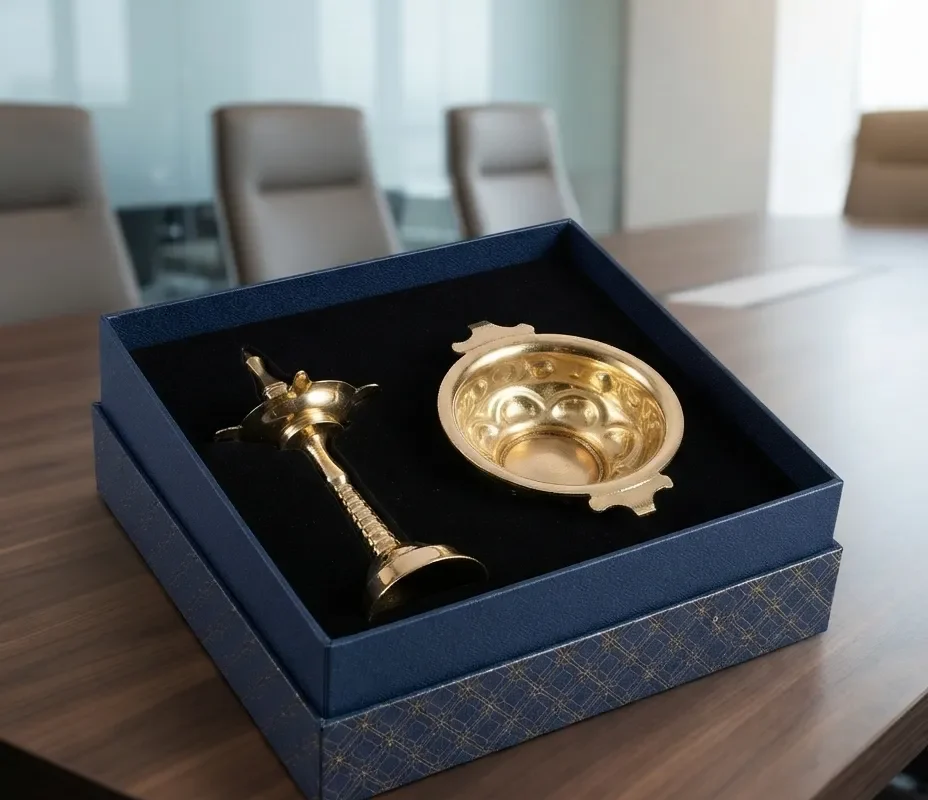 An elegant brass-tone metal ritual diya and urli featuring a patterned rigid gift box.