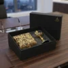 A luxury gift set featuring an ornate gold-toned metal container and a decorative diya arranged inside a branded box.