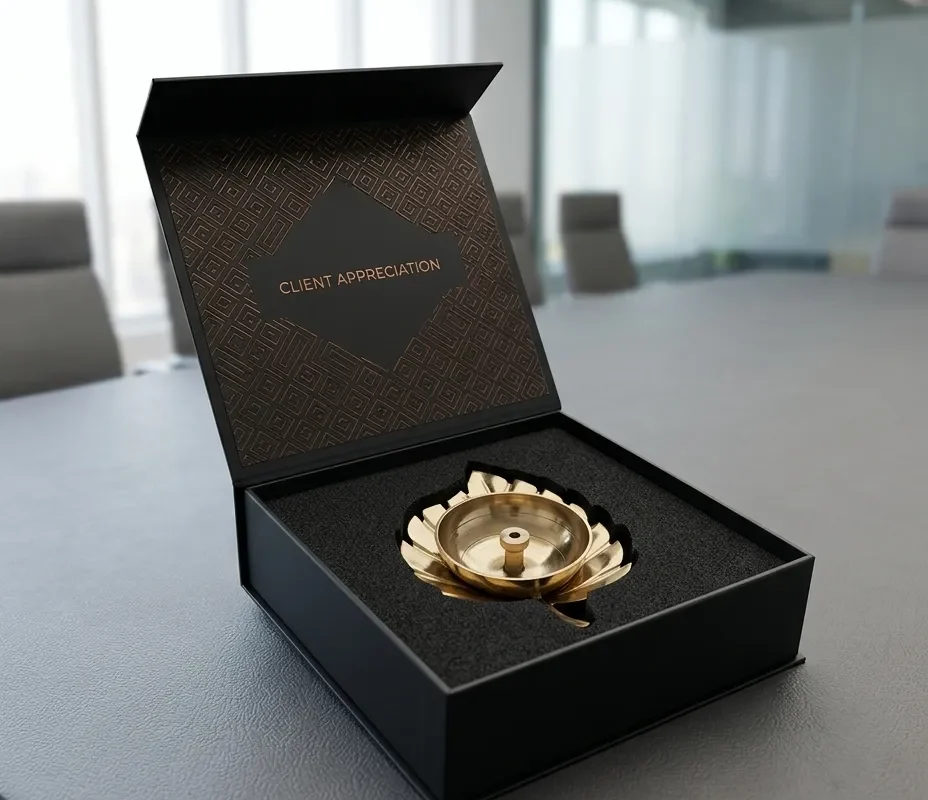 An open black gift box reveals a gleaming gold finish metal leaf diya with a central wick post.