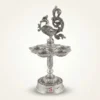 A handcrafted German silver peacock diya stand featuring intricate embossed metalwork and a traditional pedestal design.