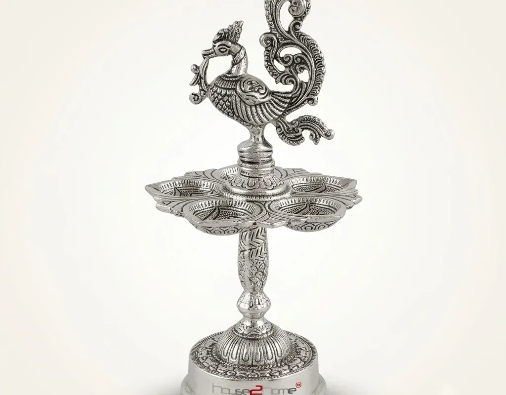 A handcrafted German silver peacock diya stand featuring intricate embossed metalwork and a traditional pedestal design.