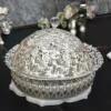 decorative silver metal bowl with an elaborate openwork design, resting on a white lotus-shaped base.
