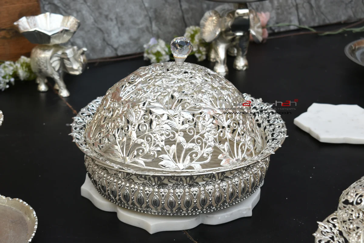 decorative silver metal bowl with an elaborate openwork design, resting on a white lotus-shaped base.