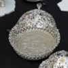 decorative silver metal bowl with an elaborate openwork design, resting on a white lotus-shaped base.