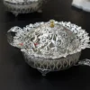 decorative silver metal bowl with elaborate cutout side handles, resting on small feet for elegance.