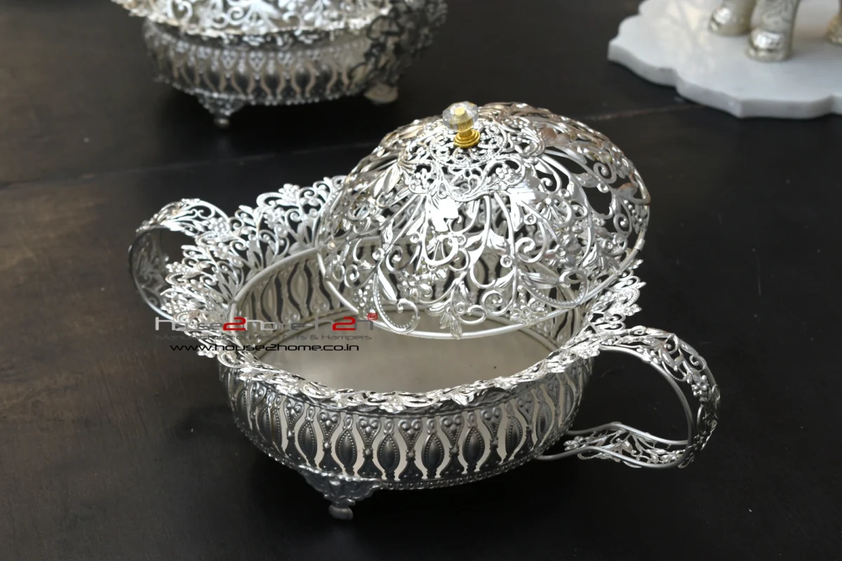 decorative silver metal bowl with elaborate cutout side handles, resting on small feet for elegance.