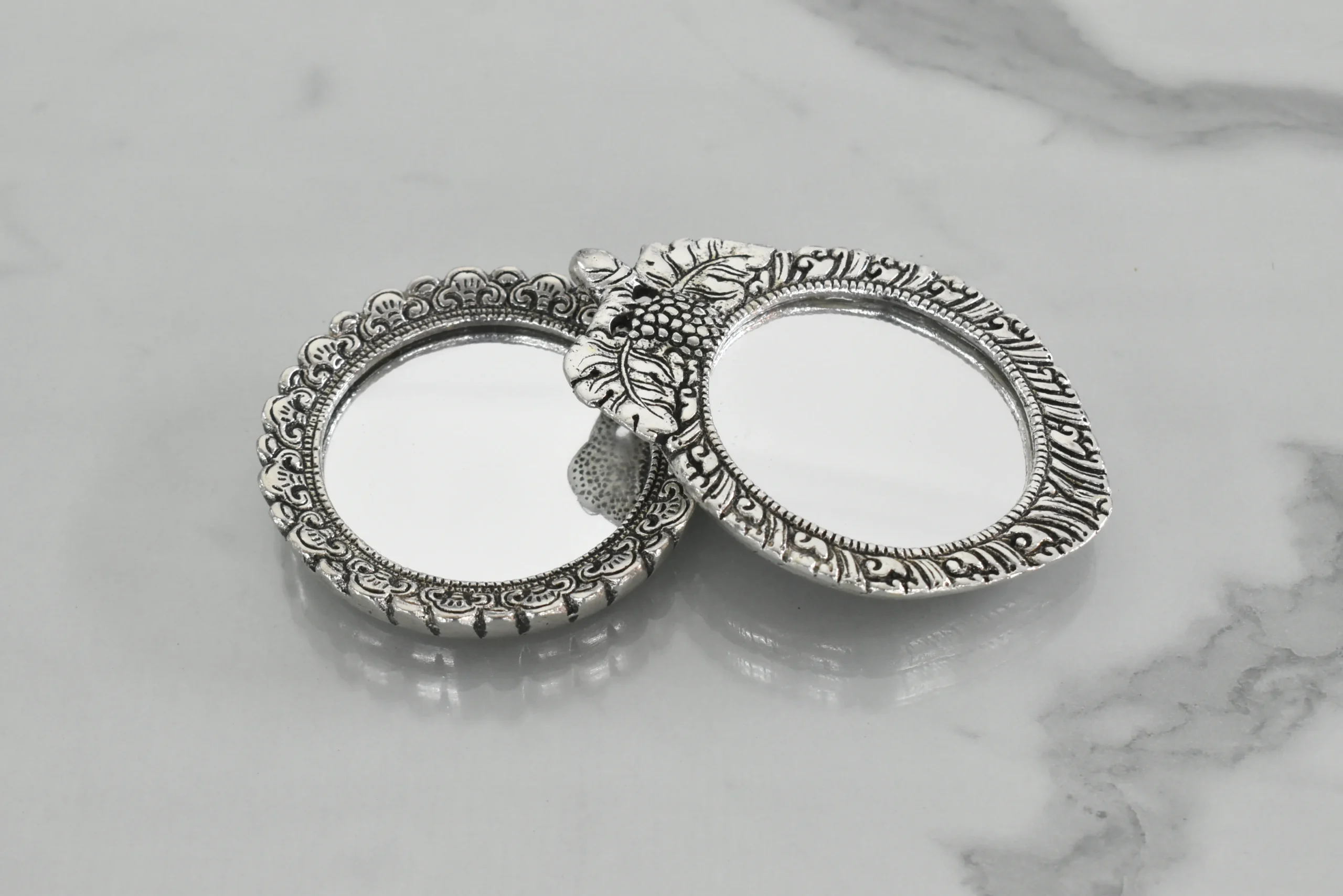 Silver-plated embossed metal pocket mirrors with ornate frames for traditional dressing and vanity decor.