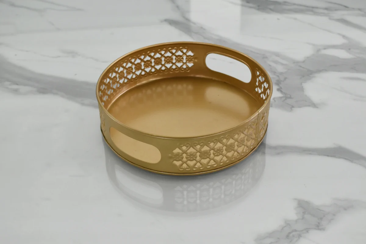 Round gold metal decorative tray with integrated cut-out handles for home styling and display.