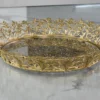 Gold-finished filigree metal round tray with intricate lace border and glass base for home styling.