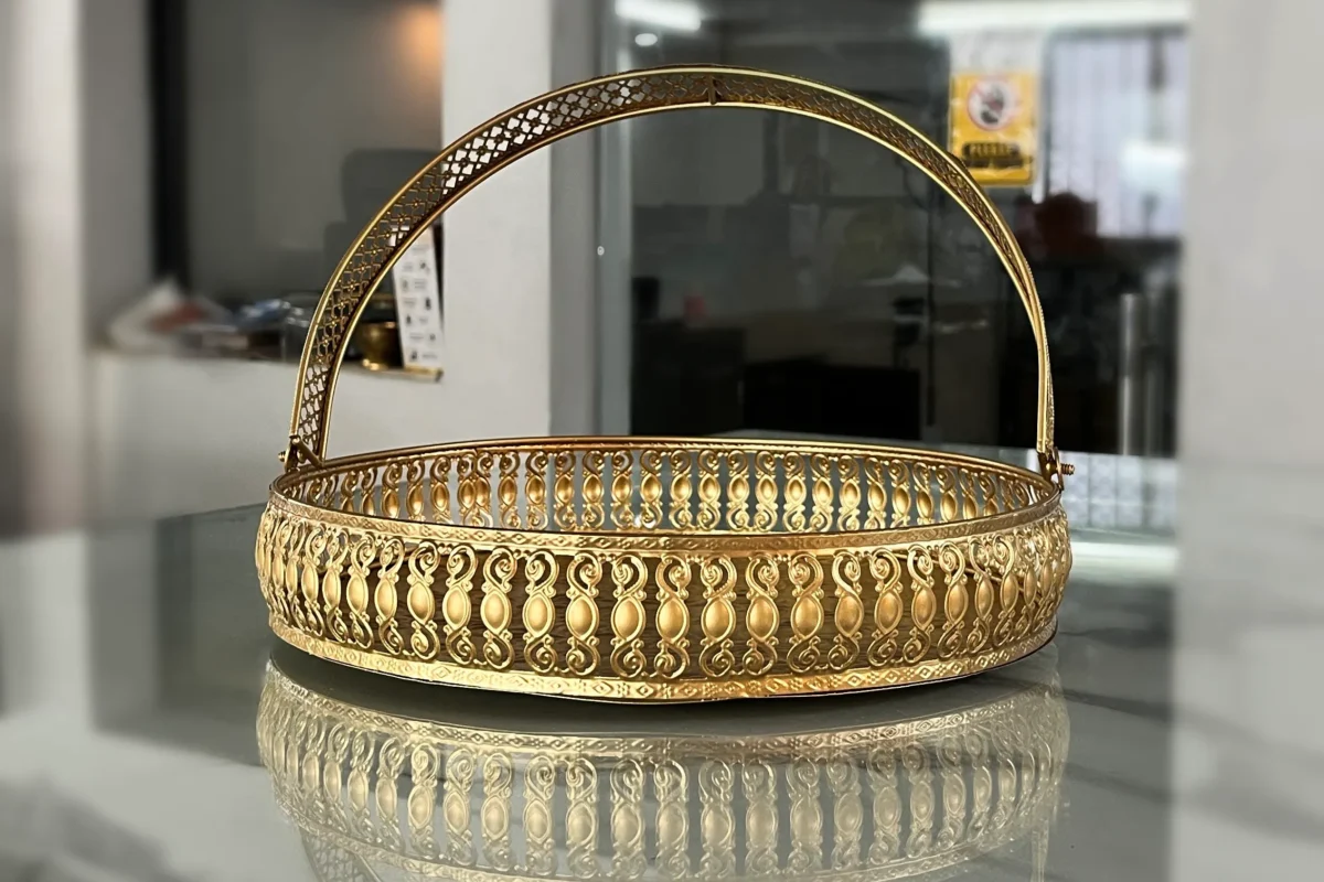 Round decorative brass basket featuring an elegant arched handle and intricate metal cutwork body detailing.
